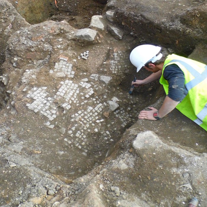 The remains of a Roman mosaic pavement is carefully uncovered. After the building was demolished, the pavement has broken and collapsed down into one of the empty foundation trenches. Credit: University of Leicester